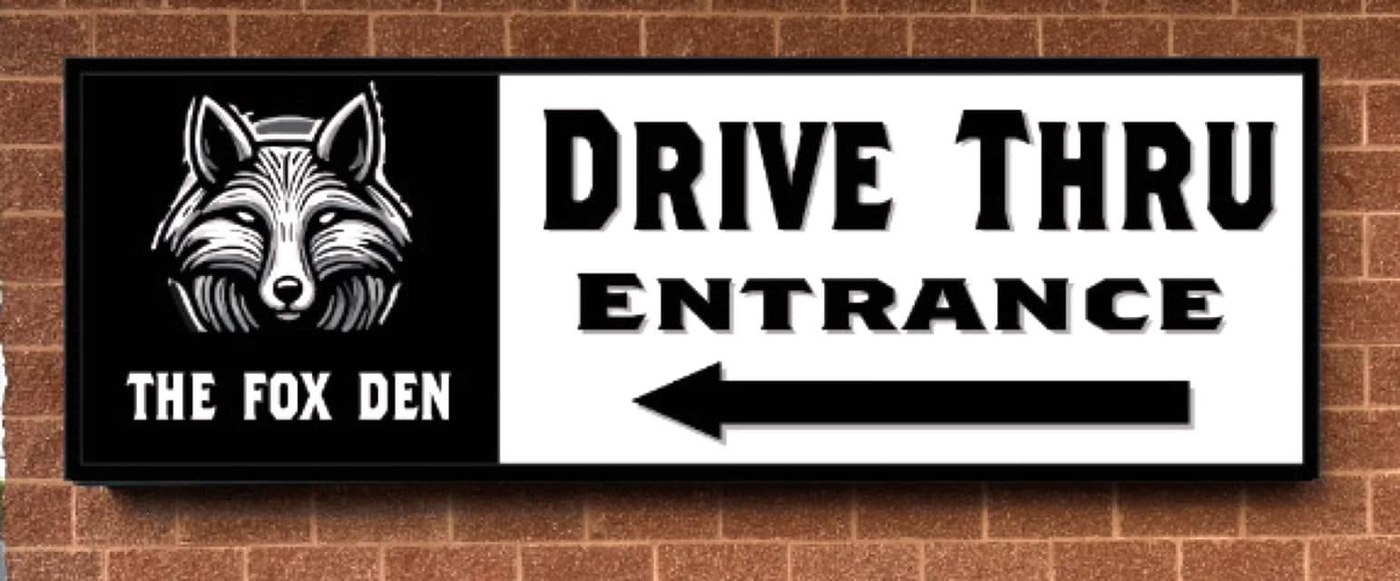 Sign on the brick wall reading The Fox Den Drive Thru Entrance with an arrow